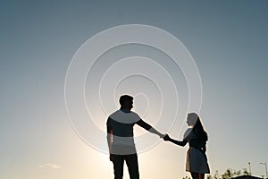 Silhouette of loving young couple dancing at sunset on background of cloudless sky in evening.