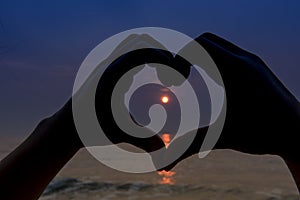 The silhouette made the heart shape from the hands at sunrise