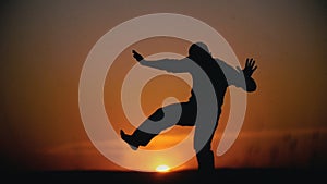 Silhouette of male acrobat performing capoeira tricks on the hill at sunset