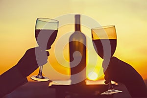 Silhouette of male and female hands toasting wine on sunset background. Romantic couple celebrating at a restaurant