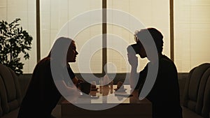 Silhouette of male and female sitting at the food bistro bar together, man drinking coffee girl talking to him.