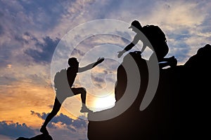 Silhouette of a male mountaineer working in a team with a partner, giving him a helping hand