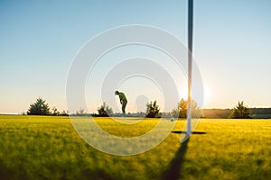 Silhouette of a male player hitting a long shot on the golf course