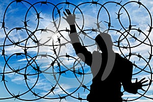 Silhouette male refugee and a barbed wire fence