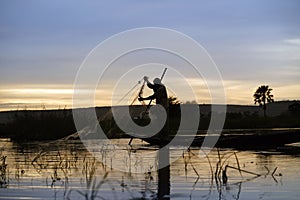 Silhouette Of A Malian Fisherman Hauling His Net Into His Boat On The Niger River At Sunset