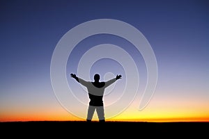 Silhouette of man with arms outstretched at sunset photo