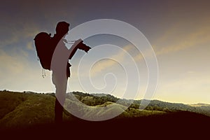 Silhouette of a man with a backpack holding the camera on the top of the hills