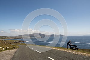 Silhouette of a man by a bench with amazing view on the ocean scenery. Achill Island, county Mayo, Ireland. Warm sunny day. Day