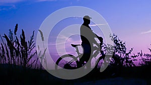 Silhouette of a man with a bicycle at blue sunset. The cyclist. Champion for life on the top