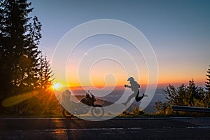 Silhouette of man biker and adventure motorcycle on the road with sunset light background. leap with joy. Top of mountains,