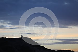 silhouette of a man in a cap sitting on a mountain watching the sunset.