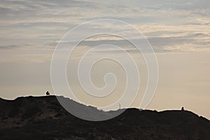 silhouette of a man in a cap sitting on a mountain watching the sunset.