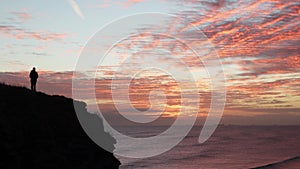 Silhouette of Man on Clifftop watching the sunrise or sunset over the sea