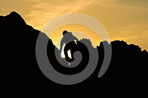 Silhouette of man climbing on rock mountain at sunset