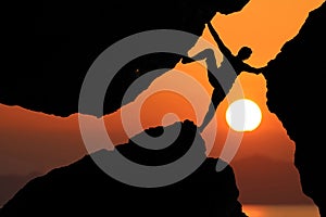 Silhouette man Climbing between rocks with red sky sunset background