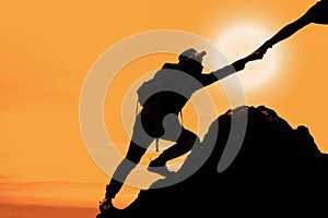 Silhouette of man climbing up mountain with hand giving help