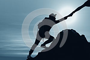 Silhouette of man climbing up mountain with hand giving help
