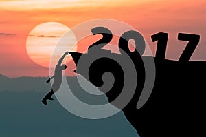 Silhouette Man climbs into cliff to the goal setting of word Happy New Year 2017 with sunset in background.