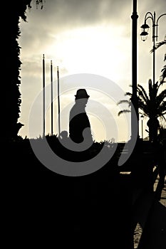 Silhouette of a man in a coat and hat on sea coast at sunset. Mystery or solitude concept. Suitable for a cover of a thriller book