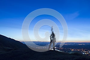 A silhouette of a man disappearing and turning into smoke. Standing on a hill. Lookng out on city lights just before sunrise