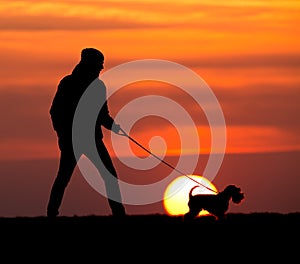 Silhouette of man with dog at sunset