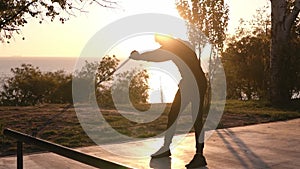 Silhouette of a man doing arm exercises outdoors using resistance band outdoors in nature. Morning sunrise, outdoors