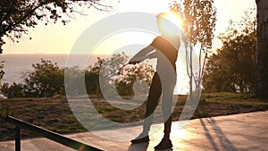Silhouette of a man doing arm exercises outdoors using resistance band outdoors in nature. Triceps exercises with rubber