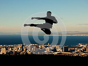 Silhouette of man doing karate with sky and city in the background. Outline of male athlete punching and kicking in the