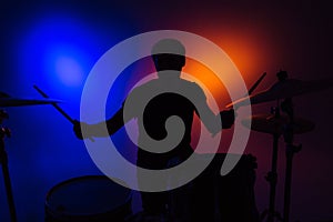 Silhouette of man drummer sitting and playing drums with sticks