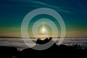 Silhouette of a man enjoying the sunrise above clouds on the mountaintop