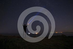 Silhouette of man with flashlight beaming ray to Milky Way galaxy