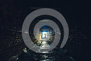 Silhouette of man with flashlight in dark dirty brick underground tunnel or sewerage corridor