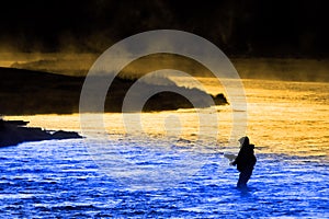 Silhouette of Man Flyfishing Fishing in River Golden Sunlight and Cool Blue Water