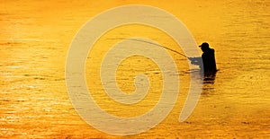 Silhouette of Man Flyfishing in River Golden Light of Early Morning with Mist