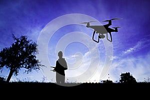 Silhouette of man with flying drone in nature at dusk.