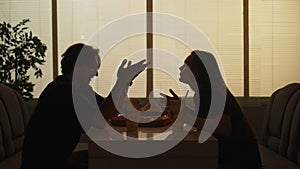 Silhouette of man and girl sitting at the bistro bar, angry conversation shouting arguing with each other, tense