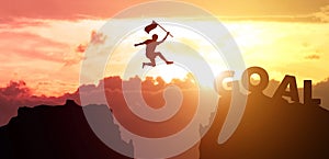 Silhouette man hand hold flag jumps from mountain to the word GOAL with sky, clouds and sunset background. Fight for reach key