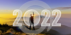 Silhouette of man hands up to challenge 2022 on mountain hill. Happy new year 2022. Man Silhouette at sunset, sunrise raise hand