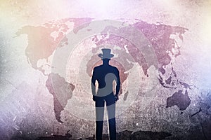 Silhouette of a man in hat standing in front of world map on grunge concrete wall