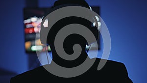 Silhouette of man in headphones playing interesting video game at home at night