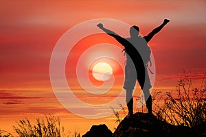 Silhouette of man hiker standing on rocky mountain peak with sunset golden sky feeling of freedom