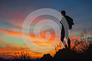 Silhouette of man hiker standing on rocky mountain peak with sunset golden sky feeling of freedom