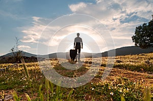 Silhouette of man and his faithful companion at sunset in the meadow bloom