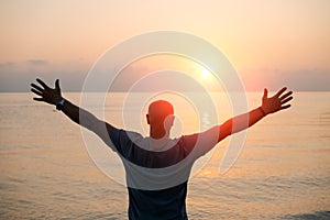 Silhouette man with his hands raised at sunset on beach arms out to sides