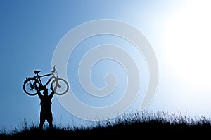 Silhouette of a man holding bicycle on blue sky