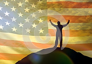 Silhouette of a man holding his hands up on the top of a mountain, against the background of the sky of the flag of America, USA.