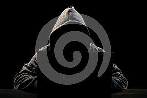 Silhouette of a man in a hood on a black background, his face is not visible, he sits at the computer. The concept of a criminal,