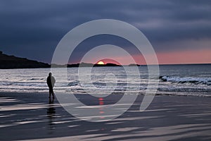 Silhouette of Man in Hoodie Walking Alone on Beach During Sunset