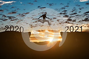 Silhouette of man jump on the cliff between 2020 to 2021 years over sunset or sunrise background.