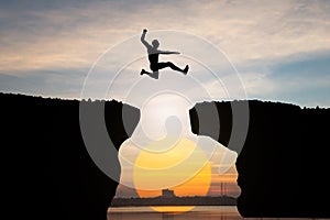 Silhouette of Man jump through the gap between hill on sunset background, business concept idea